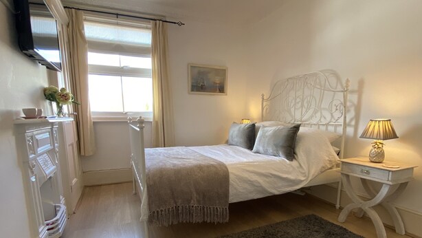 Un dormitorio con cama, mesita de noche, lámpara y ventana con cortinas.