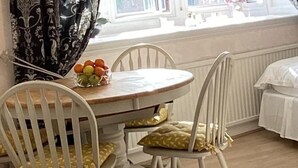 Un comedor con una mesa redonda, dos sillas blancas con cojines amarillos y un frutero sobre la mesa.
