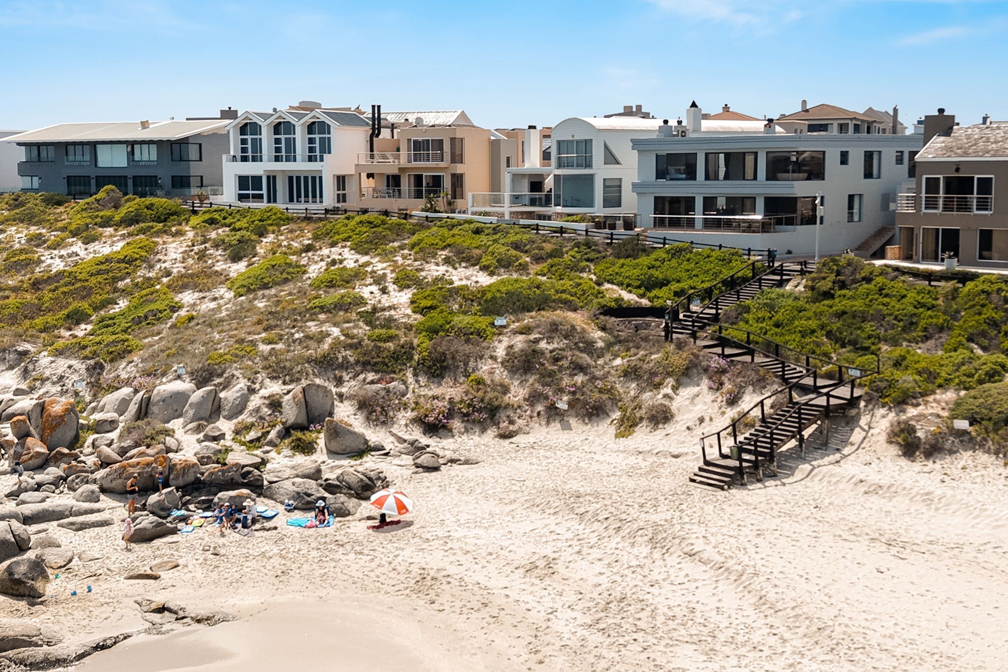 Une propriété située en bord de mer, avec un escalier menant à une maison, une plage de sable et un terrain rocheux.
