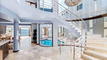 Un ampio interno con una scala a forma di ferro di cavallo, una zona piscina e vista sul mare.