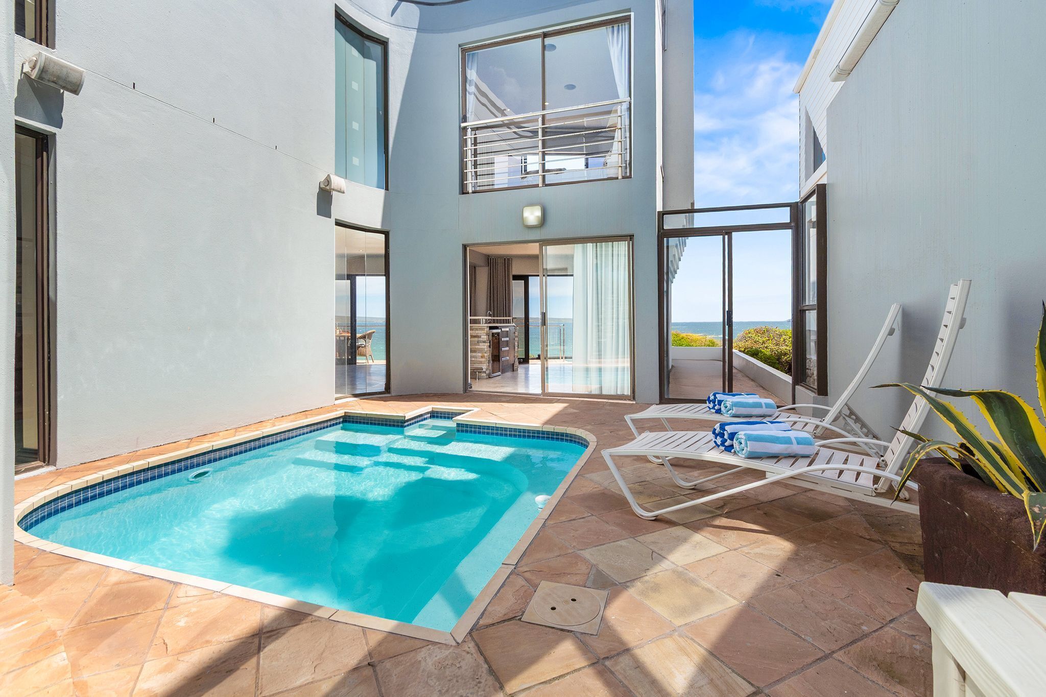 A modern pool area with a clear blue pool, lounge chairs, and a view of the sea.
