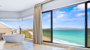 Een moderne badkamer met een groot bad, uitzicht op de oceaan en een groot raam met gordijnen.