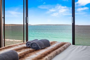 A room with a large window overlooking a body of water and distant land. - Tenos On Calypso 16 (Langebaan)