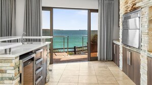 Een moderne keuken met een grote schuifglazen deur die leidt naar een balkon met uitzicht op zee.