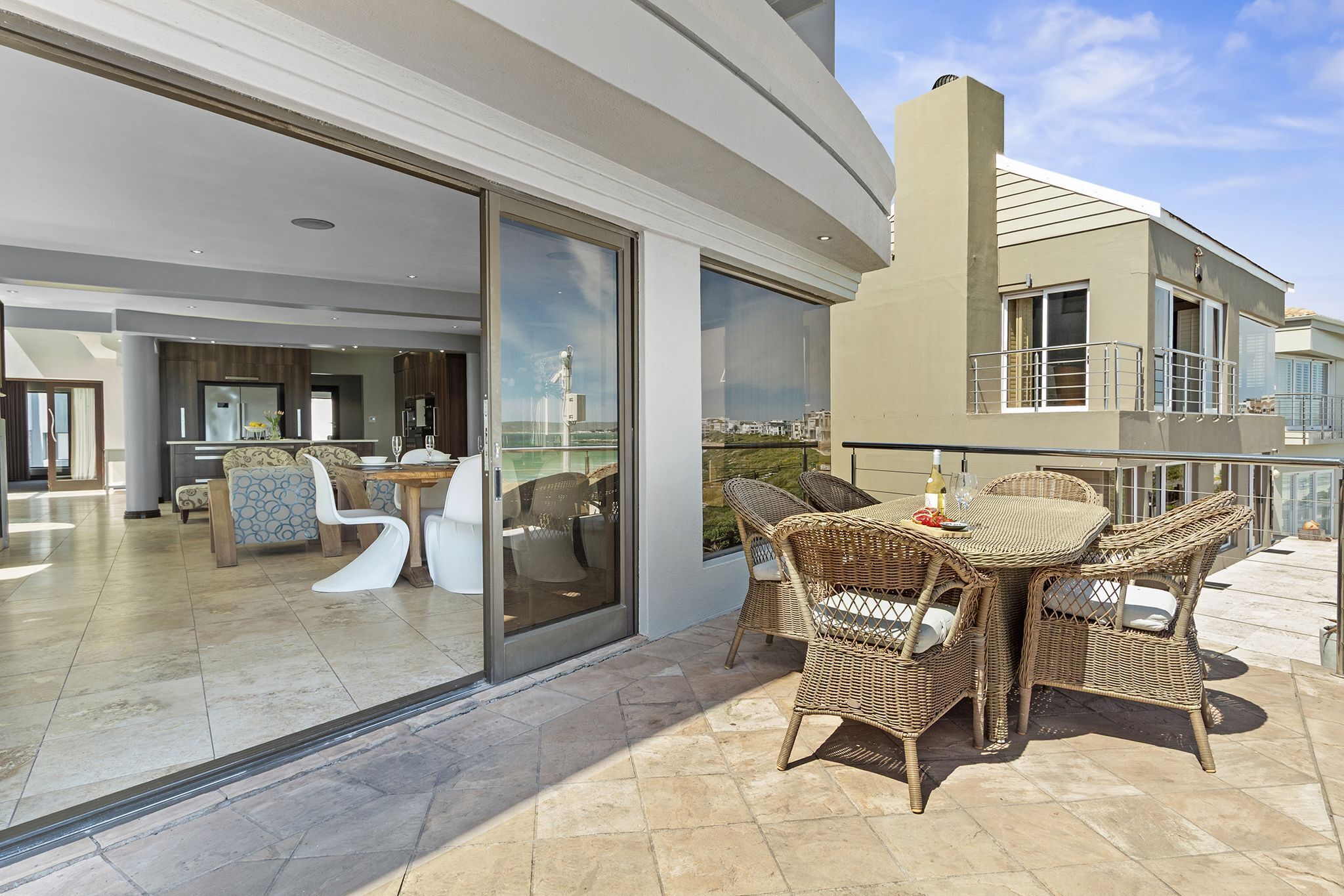 A modern outdoor dining area with wicker furniture and a glass door leading to an indoor space.