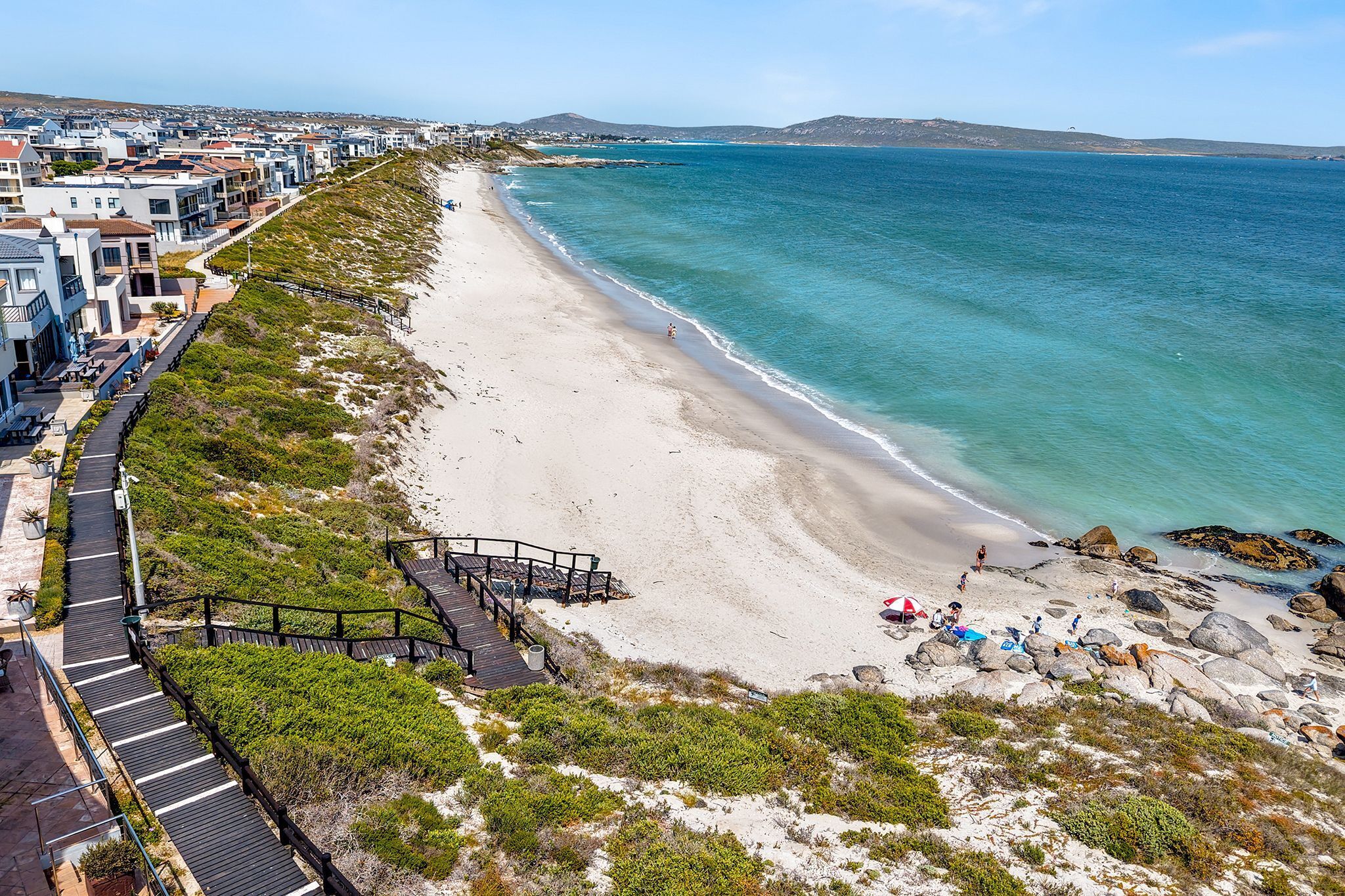 A coastal area with a beach, a wooden boardwalk, and buildings along the shore.