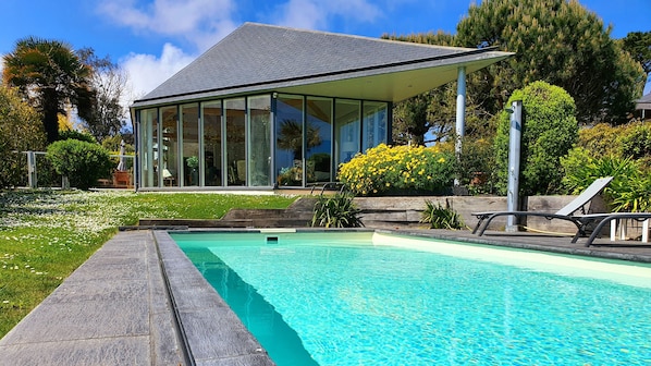 A modern house with a swimming pool, surrounded by lush greenery and a clear blue sky.
