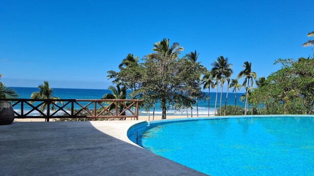 Une piscine d’un bleu éclatant, dotée d’une terrasse en bois et offrant une vue sur la plage et l’océan.