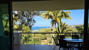Un balcon avec une table et des chaises, donnant sur un paysage côtier agrémenté de palmiers et offrant une vue sur la mer.