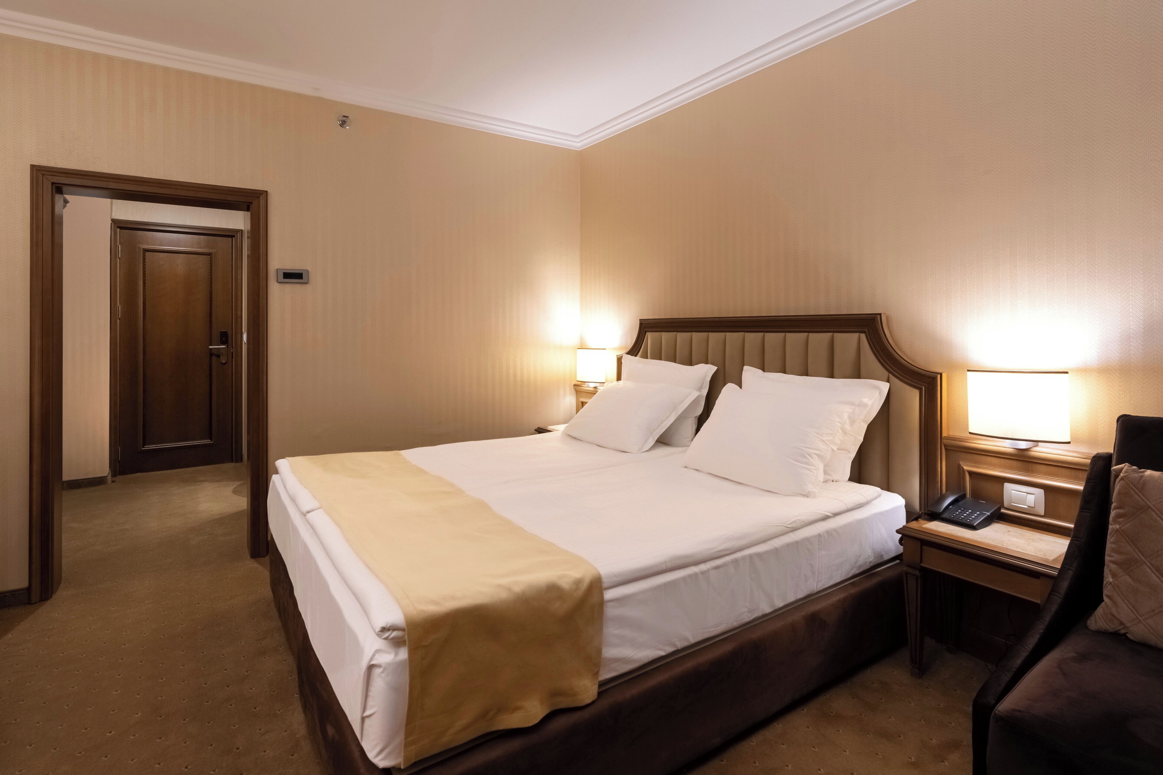 A hotel room with a large bed, bedside tables with lamps, a desk, and a chair.
