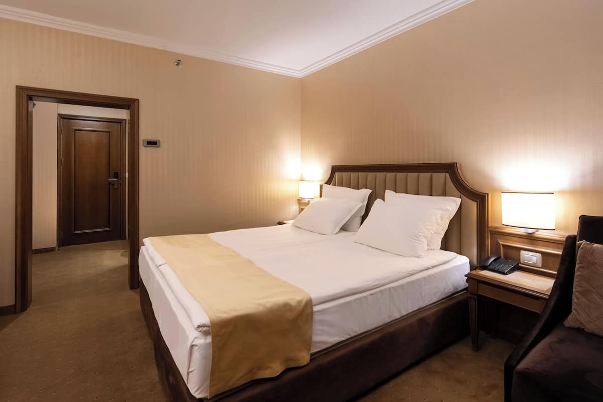 A hotel room with a large bed, bedside tables with lamps, a desk, and a chair.