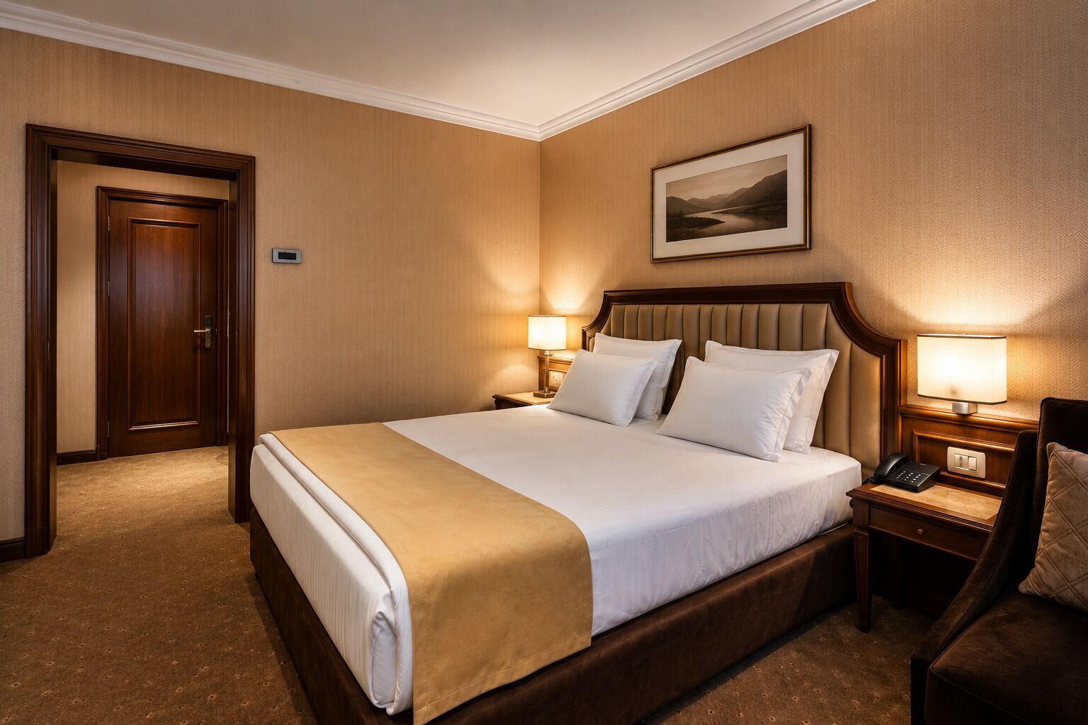 A hotel room with a large bed, two bedside tables, a nightstand, a chair, and a framed picture on the wall.