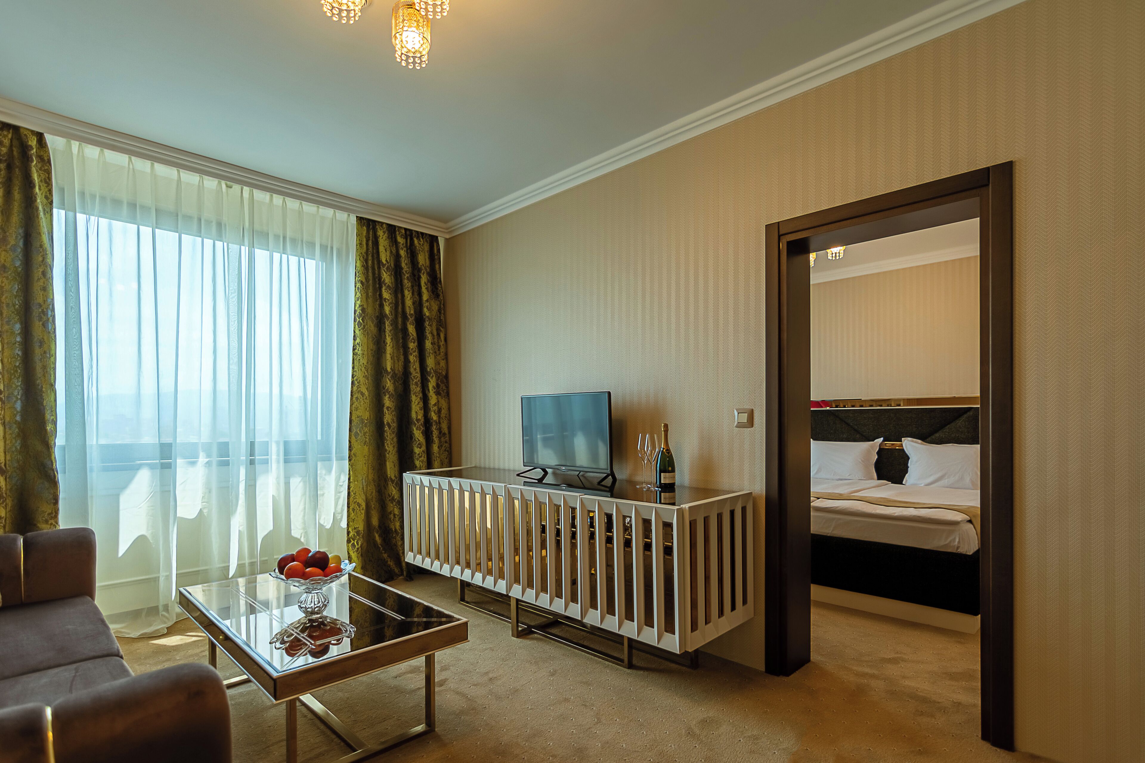 Habitación de hotel con cama, televisor, una mesita de vidrio con fruta y vistas al exterior.