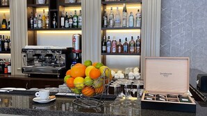 Zona de bar con estantes llenos de botellas de licor, una máquina de café y un frutero.