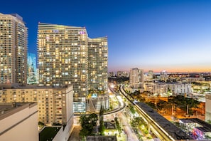 A high-rise building with multiple floors and balconies, surrounded by other buildings and a busy road with moving vehicles.