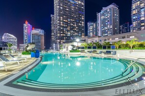 Une piscine dotée de chaises longues et offrant une vue sur les gratte-ciel la nuit.
