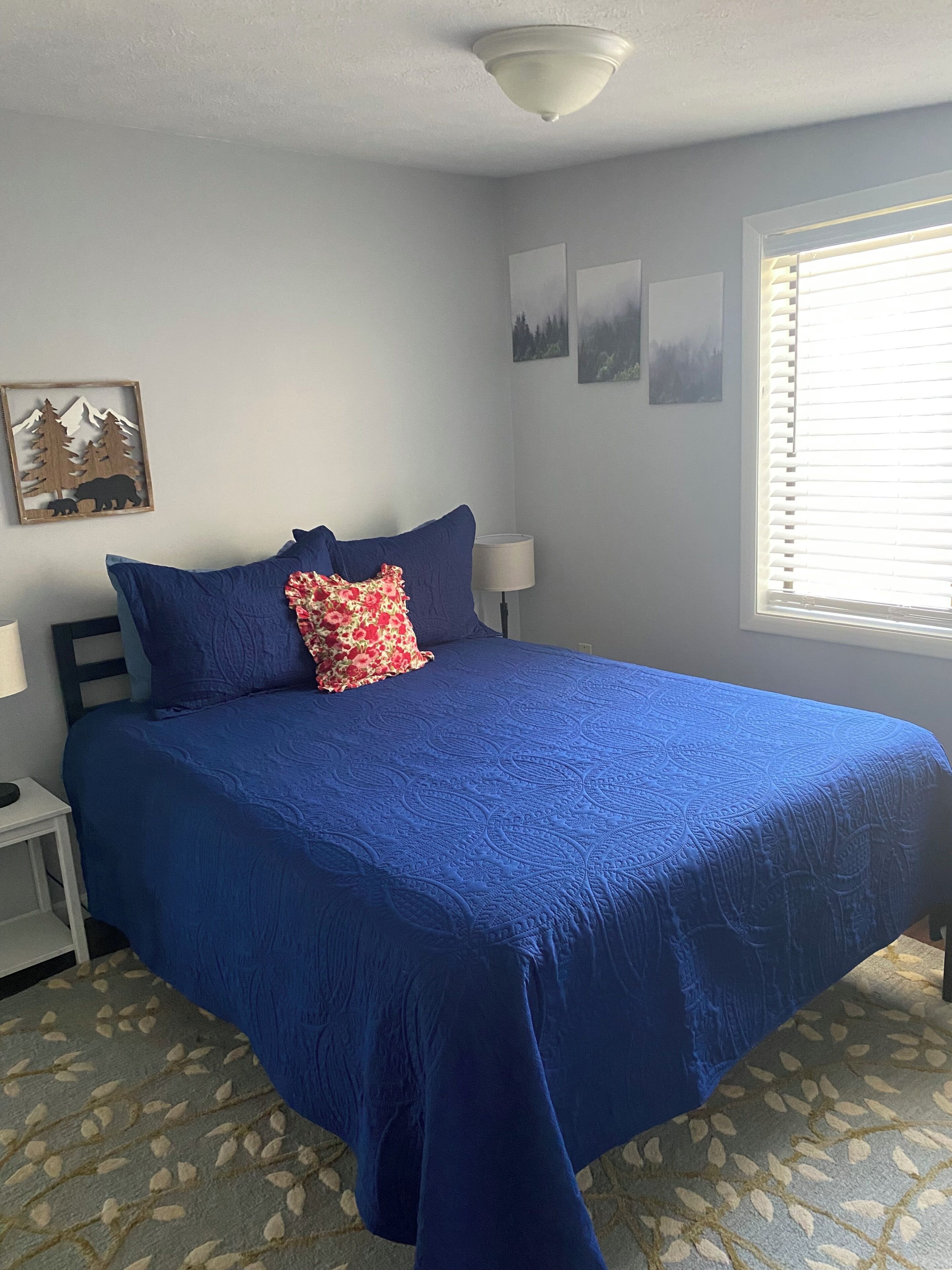 A bedroom with a large bed, a nightstand, a lamp, and a window with blinds.