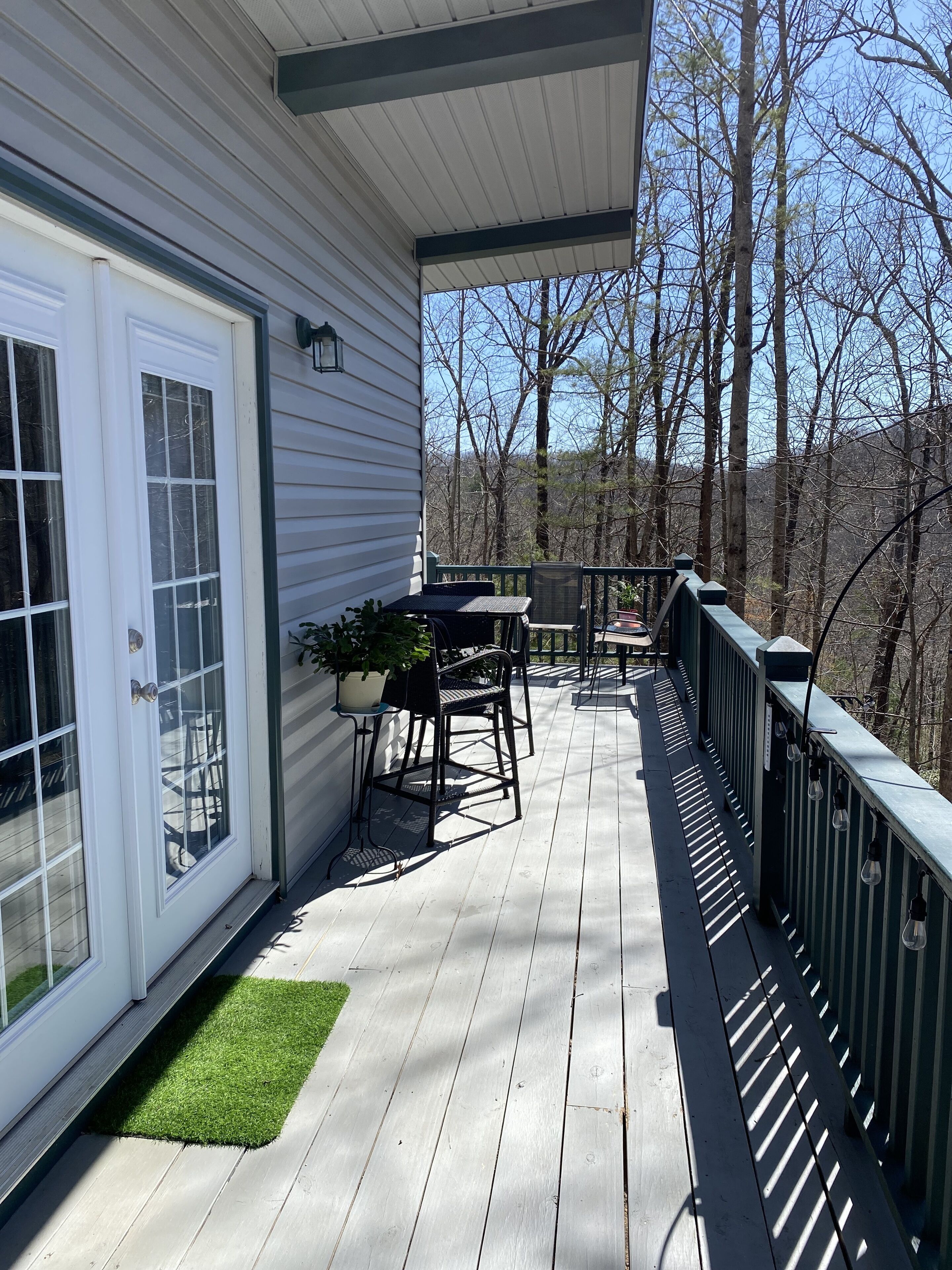 A covered deck with a table and chairs, a potted plant, and a view of trees and hills.