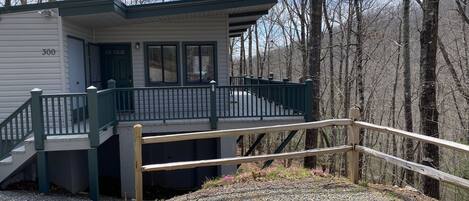 A small cabin with a porch and a wooden fence, surrounded by trees.