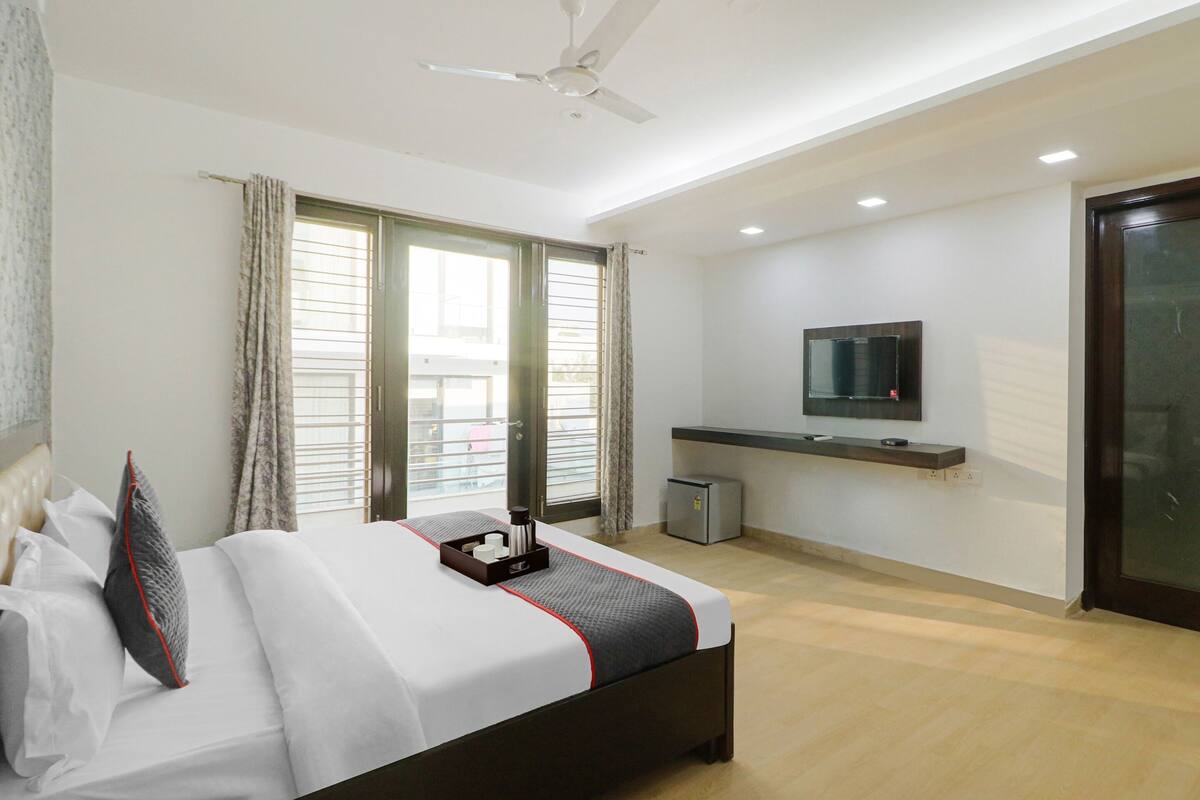 A modern hotel room with a large bed, a ceiling fan, a TV mounted on the wall, and a small desk with a lamp.
