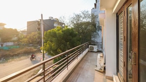 Un balcón con barandilla metálica, vista a una carretera con una motocicleta, y un edificio con fachada blanca y una ventana con marco metálico.