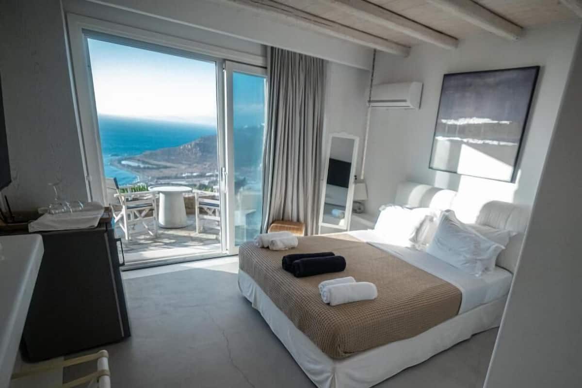 Een hotelkamer met een groot bed, een bureau, een stoel en uitzicht op zee.