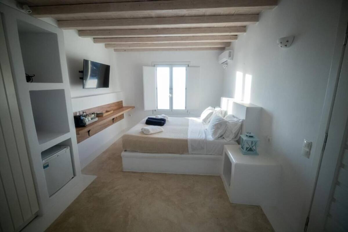 Een slaapkamer met een bed, een televisie, een raam en een klein nachtkastje.