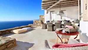 A seaside patio with wicker furniture, a stone wall, and a view of the ocean. - White Rock Suites & Villas (Mykonos)