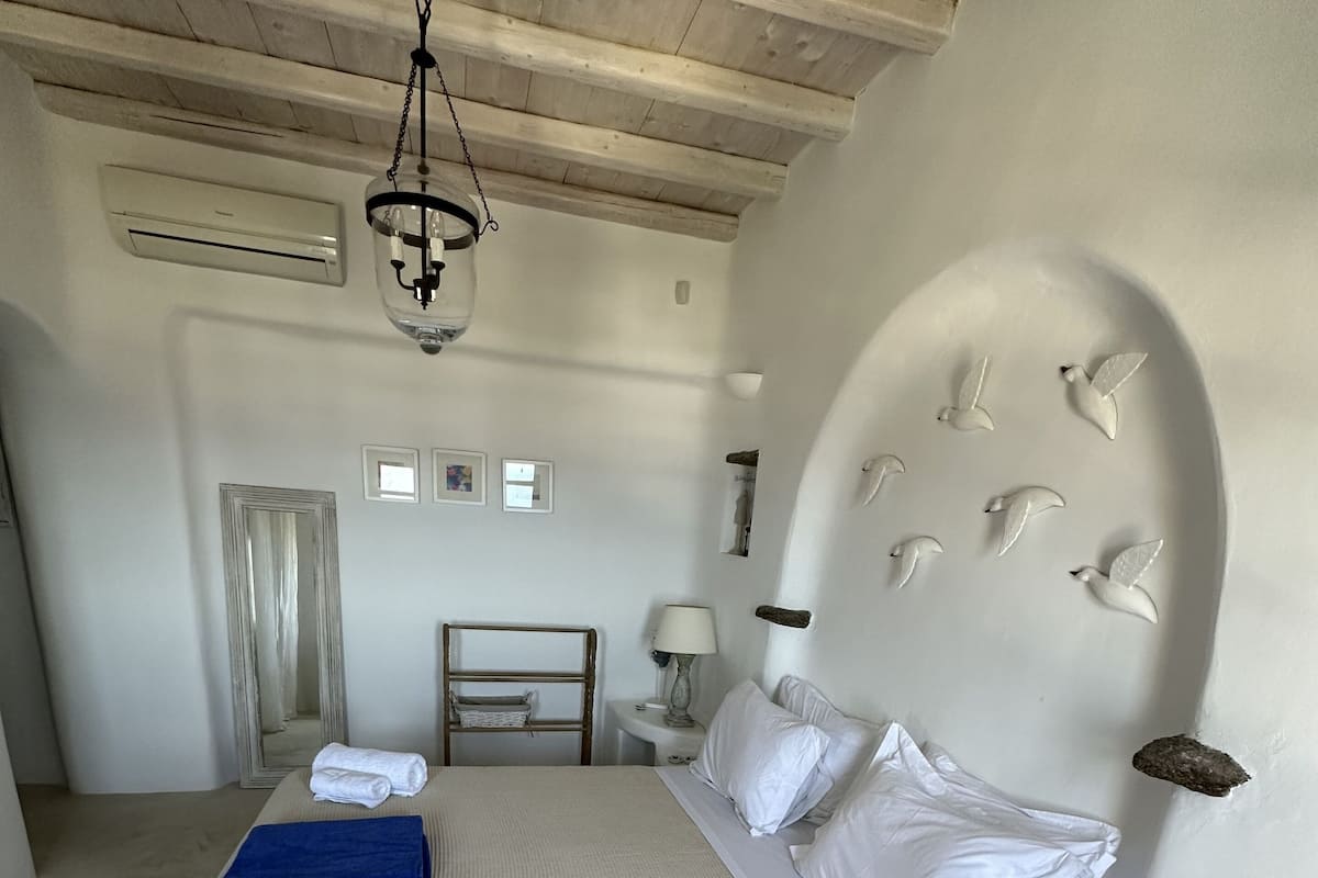 Een slaapkamer met een groot bed, een nachtkastje, een lamp en een plafondlamp.