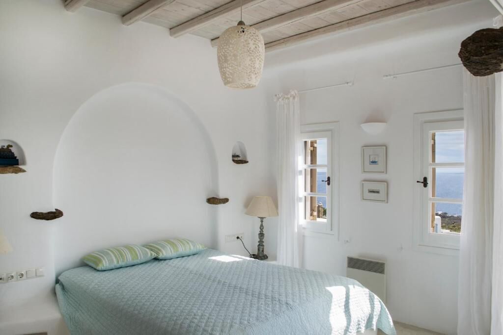 Un dormitorio con cama, lámpara, ventana y vista al mar.