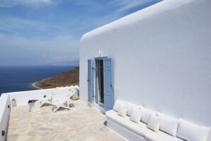 Un edificio blanco con puerta azul, suelo de piedra y sofá blanco con cojines.