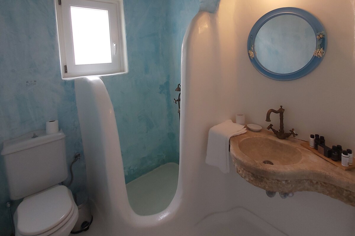 Een badkamer met een wit toilet, een wastafel met een stenen aanrechtblad, een spiegel en een raam boven het toilet.