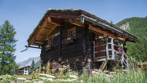 Un chalet rustique en bois doté d’un balcon, entouré d’une végétation luxuriante et avec des montagnes en toile de fond.