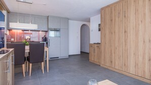 Une cuisine moderne avec des meubles gris, un coin repas avec deux chaises et un meuble en bois doté de poignées.