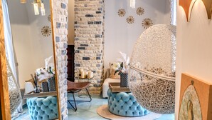 A room with a brick wall, a large mirror, a blue cushioned bench, a hanging light fixture, and a decorative globe.