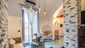 A cozy living room with a stone wall, a cushioned sofa, a hanging chair, and a wooden coffee table.