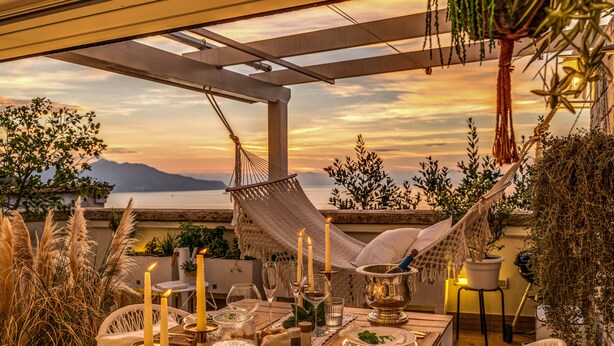 A sunset dining area with a table set for two, candles, and a hammock.