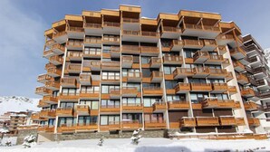 A multi-story hotel with balconies, a stone facade, and a snowy mountain backdrop. - 100m from ski slopes, 1st floor, terrace, balcony, tv, 90m², Val Thorens (Val Thorens)