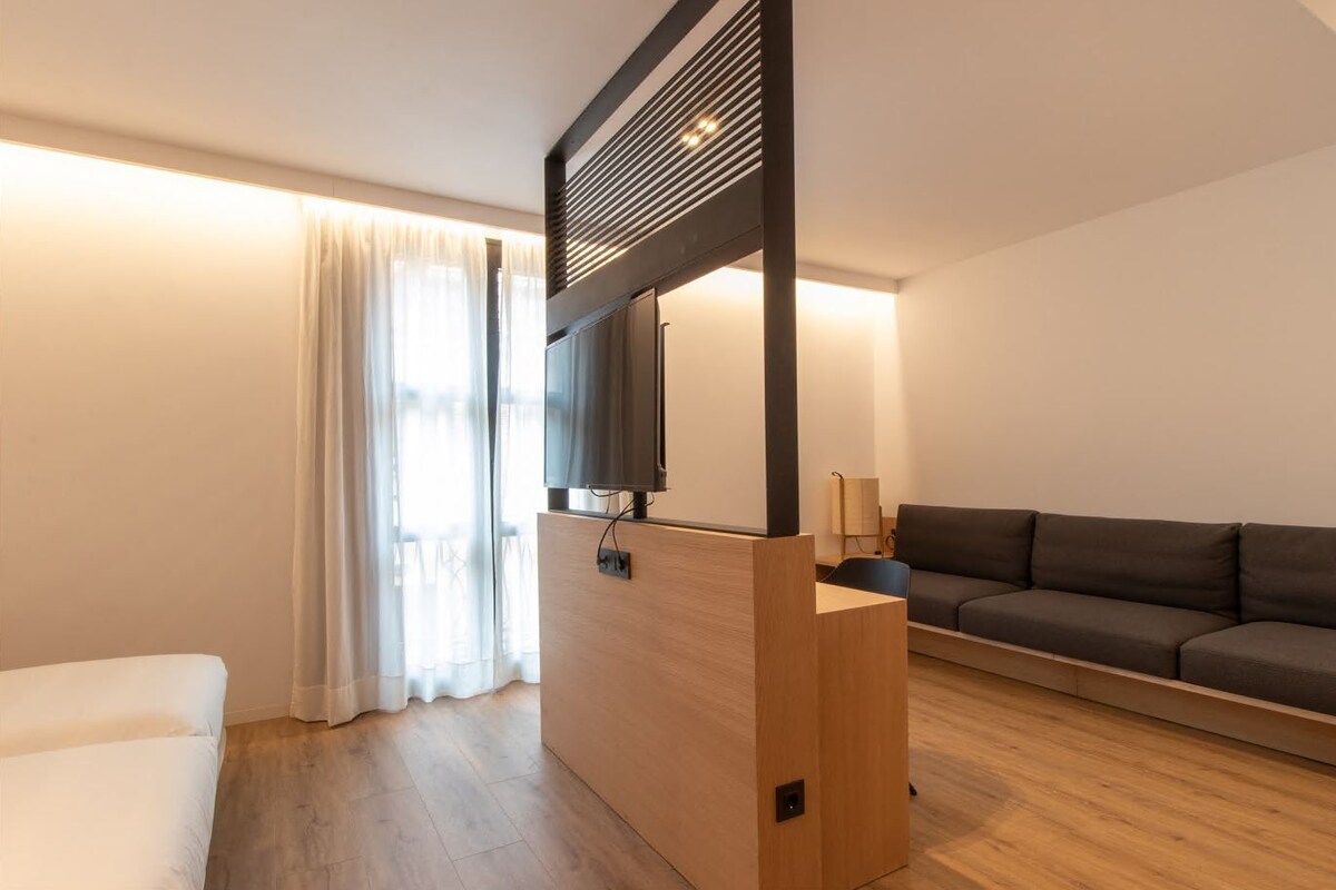 Una sala de estar moderna con una pared de acento de madera, un televisor de pantalla plana montado en ella, un sofá oscuro y un sillón blanco.