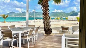 Un patio al aire libre con una mesa, sillas, una palmera y vistas a la playa y las montañas.
