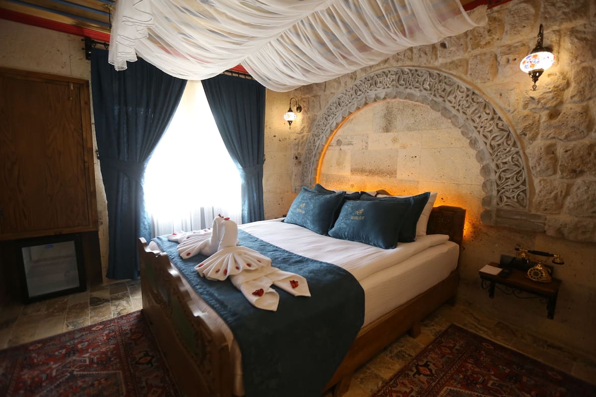 Quarto de hotel com cama, guarda-roupa de madeira, parede de pedra e arco decorativo.