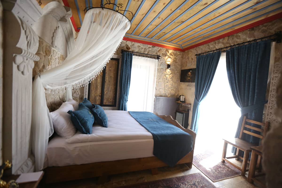 Quarto com cama, cadeira, mesa e janela com cortinas.