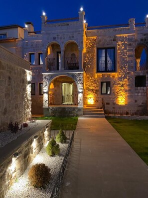 A stone building with arched windows and a central entrance, surrounded by a well-maintained garden and pathway. - Akritis Cappadocia House (Nevsehir)