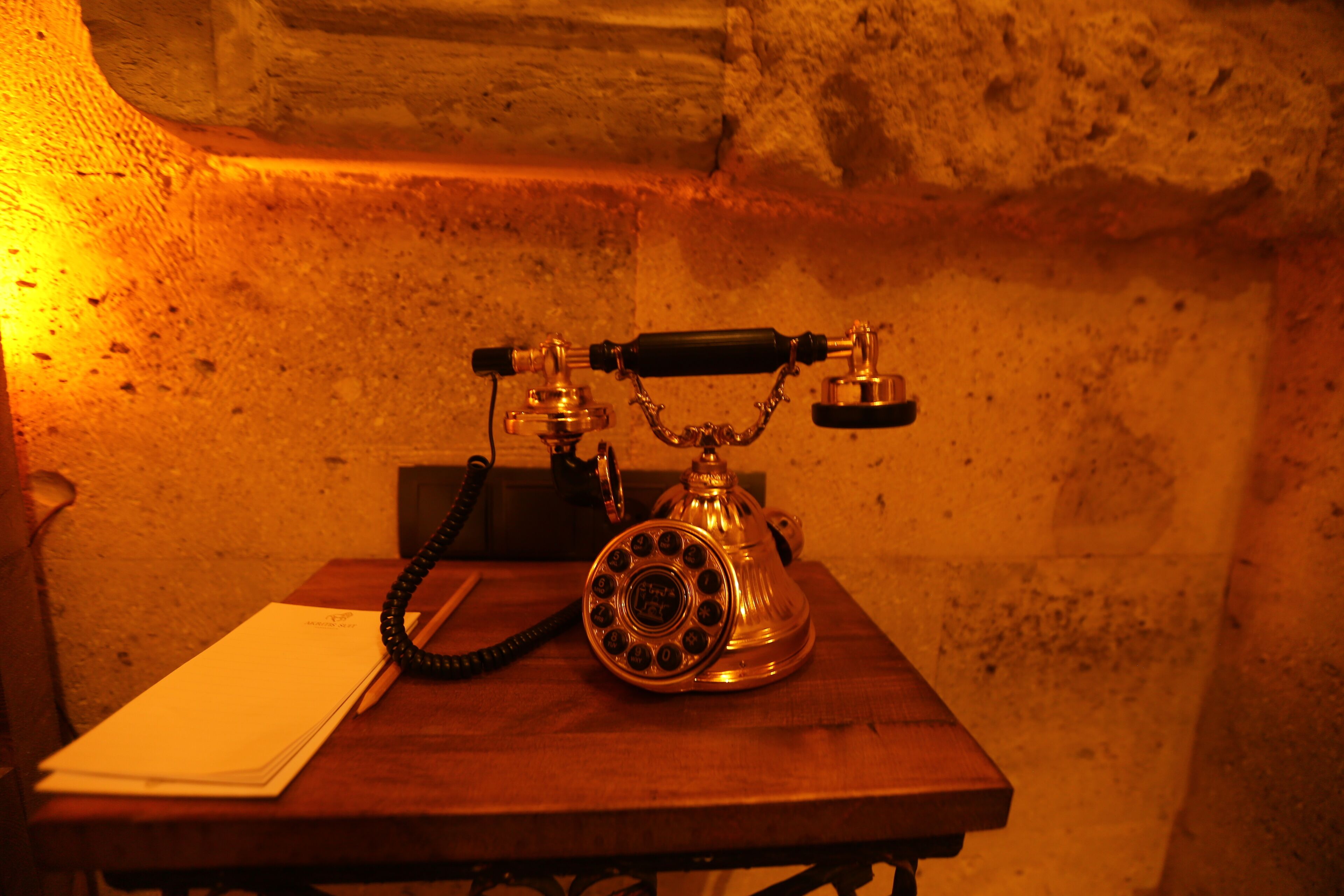 A vintage rotary dial telephone on a wooden table in a room with textured walls.