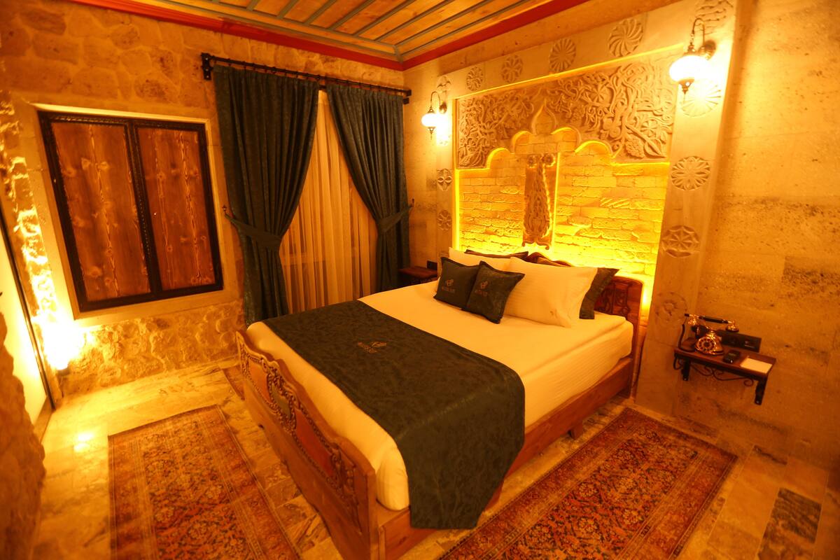 Quarto com cama grande, mesa de cabeceira, luminária na parede e cabeceira decorativa.