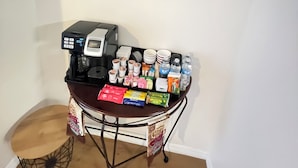 Una estación de café con una cafetera, tazas y diferentes cápsulas de café.