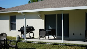 Un patio techado con una parrilla, muebles de exterior y un jardín cercado.