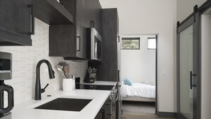 Cuina moderna amb encimera blanca, armaris foscos i microones. També es veu un rentaplat amb un aixeta i un suport per ganivets.