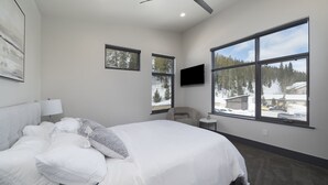 A modern bedroom with a large bed, a ceiling fan, a TV, and large windows offering a view of a snowy landscape.