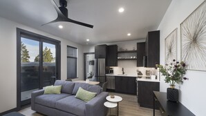 Una cocina moderna con muebles oscuros, un refrigerador de acero inoxidable y un comedor con un sofá gris y una pequeña mesa redonda.